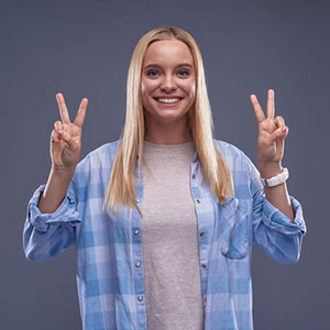 Charming young lady in blue shirt showing victory gesture