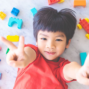 Happy boy surrounded by colorful toy blocks top view V shape hand for victory